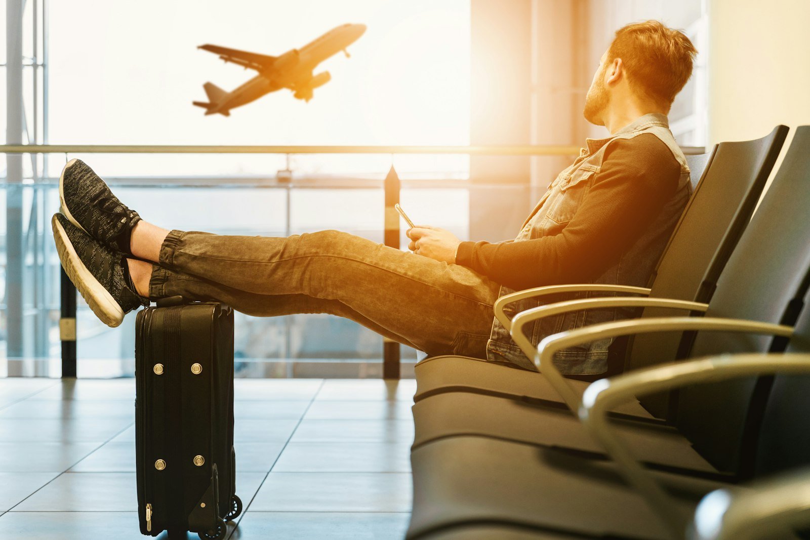 Man sitting on gang chair with feet on luggage looking at airplane