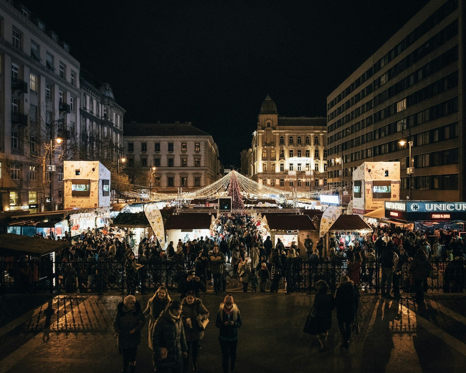 Visitors browsing lit Christmas market stalls at night