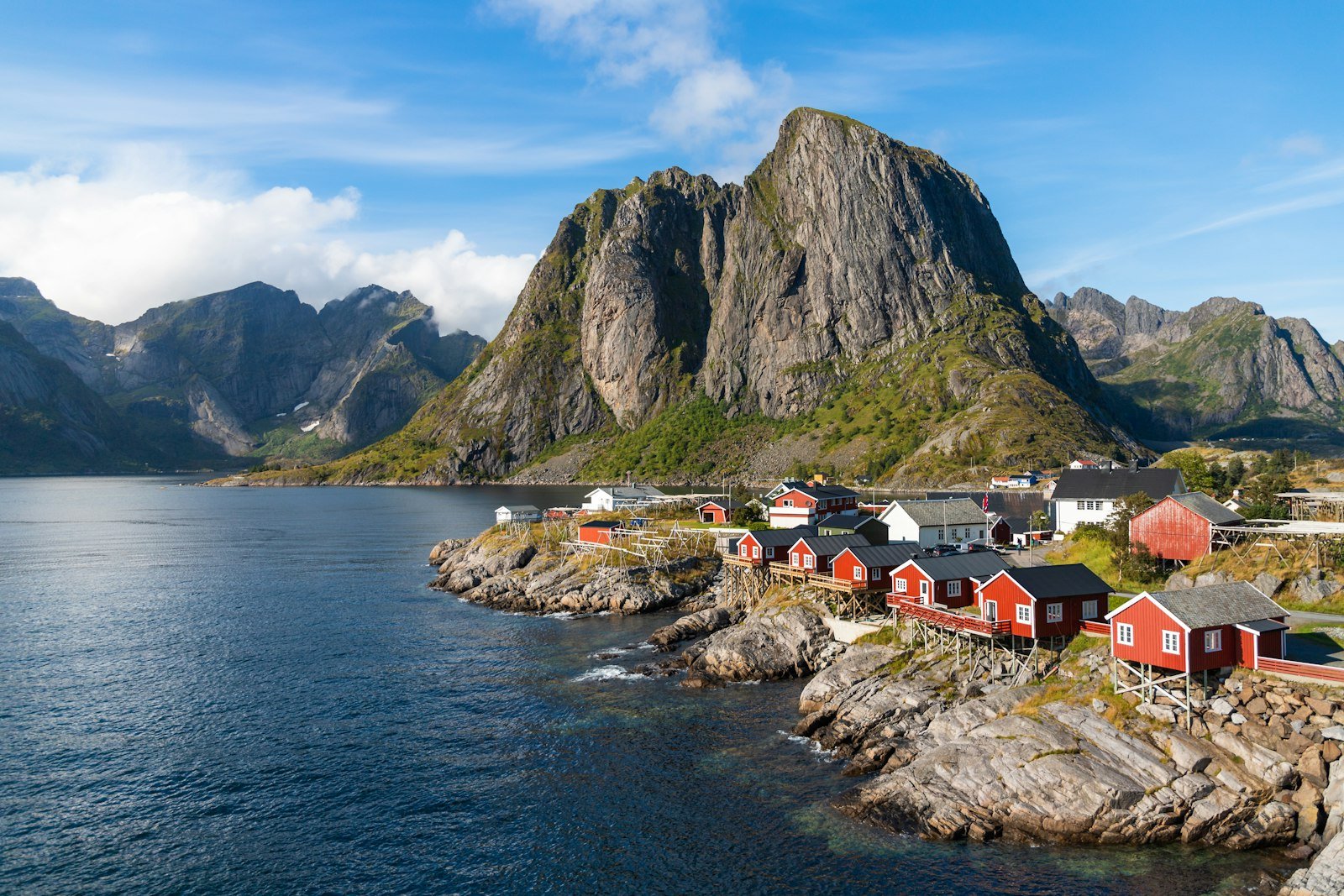 A group of houses by a body of water with mountains in the background with Lofoten in the background, Hamnøy, Norway